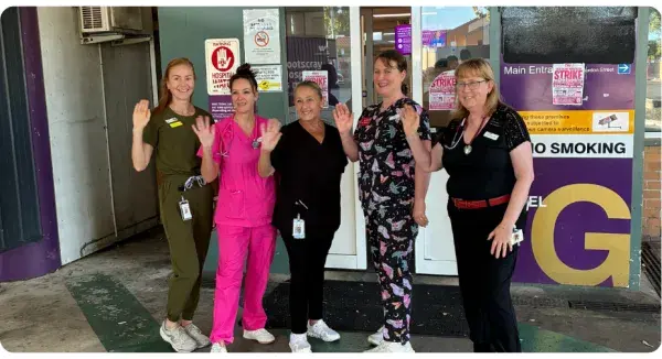 5 women smiling and waving outside a doorway.