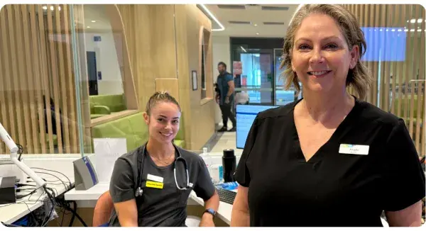 2 women smiling, one standing, one sitting.