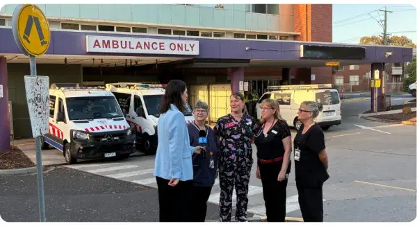 Four hospital women being interviewed by a female reporter in front of ambulances in the 'Ambulance Only' bay.