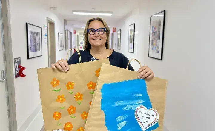 Director of Nursing is holding two bags in a corridor that have illustrations done by children