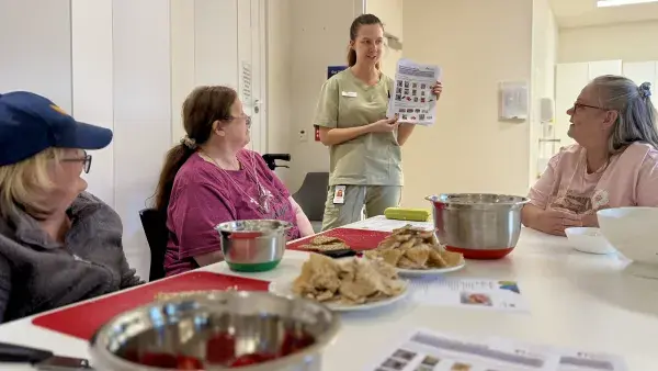 Supporting the community beyond the hospital. Dietitians smiling holding brochure talking to ladies about healthy eating around a kitchen table