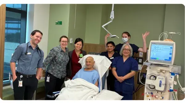 Hospital team of 6 surrounding a man in a hospital bed with monitor nearby.