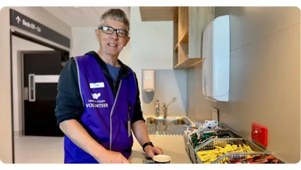 Man smiling next to a drink in a kitchen wearing a purple Western Health volunteer vest.